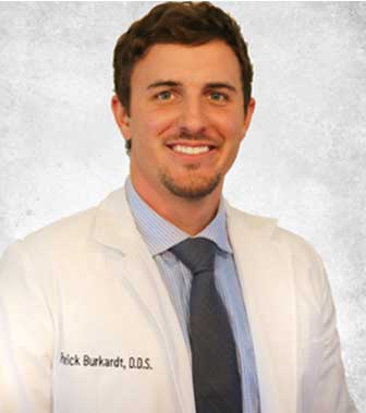 Portrait of Dr. Patrick Burkardt in a white coat with his name and D.D.S. title embroidered on it